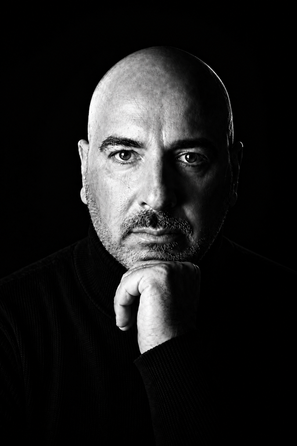 Portrait noir et blanc de Romain Giaretti, pull sombre, main sous le menton, fond noir